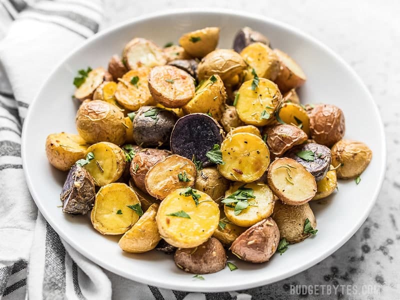 Front view of Rosemary Roasted Potatoes in a white bowl with chopped parsley sprinkled over top. 