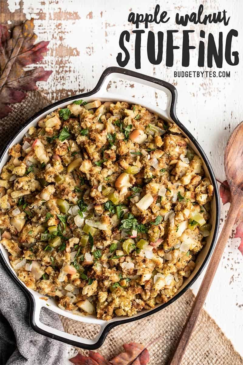 A casserole dish full of Apple Walnut Stuffing with a wooden spoon on the side