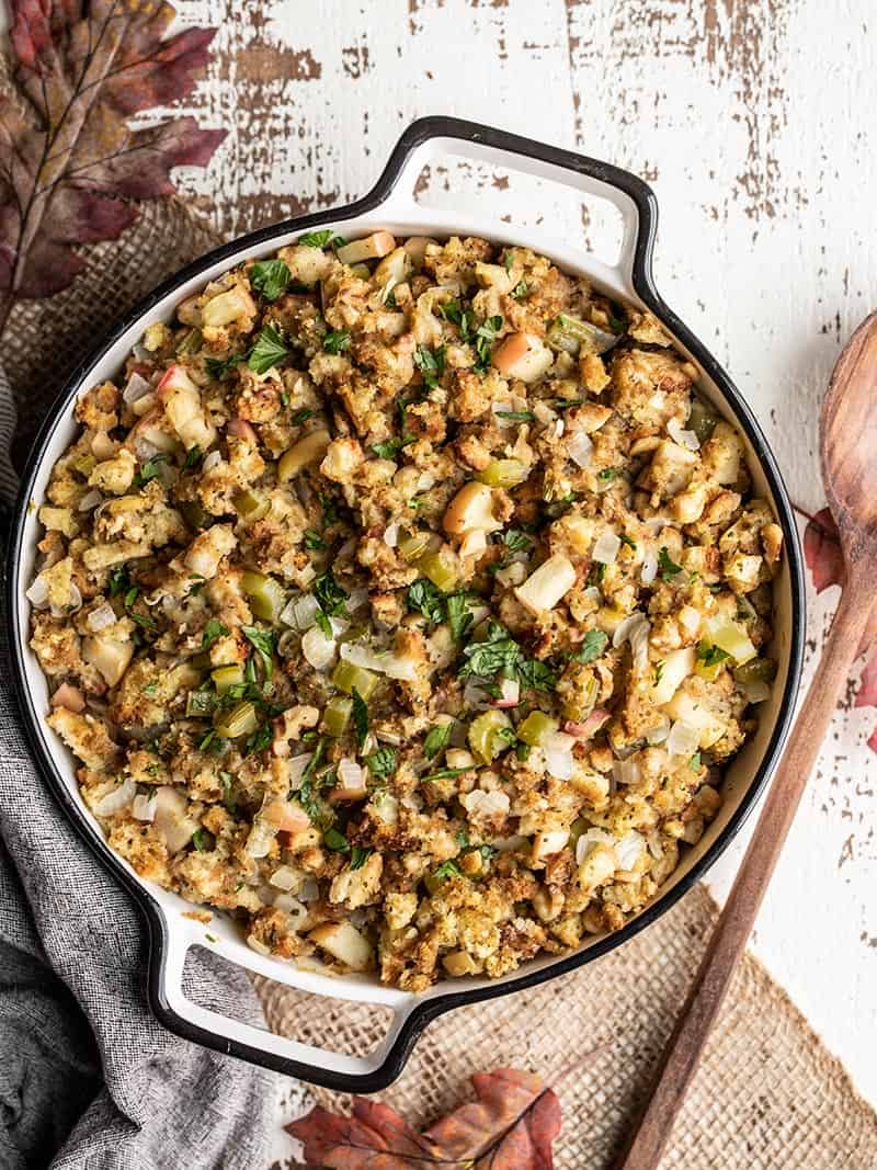 A casserole dish full of Apple Walnut Stuffing with a wooden spoon on the side