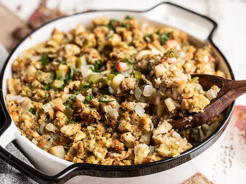 Close up side view of Apple Walnut Stuffing in the casserole dish, being scooped out with a wooden spoon.