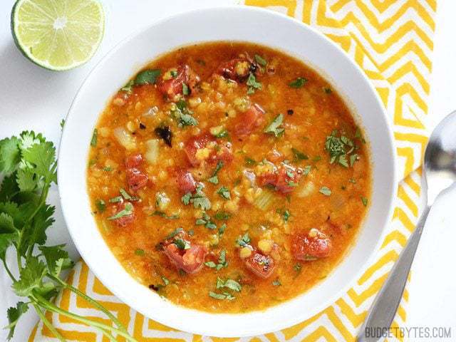 Above view of Mexican red lentil stew in a bowl alongside lime and coriander.