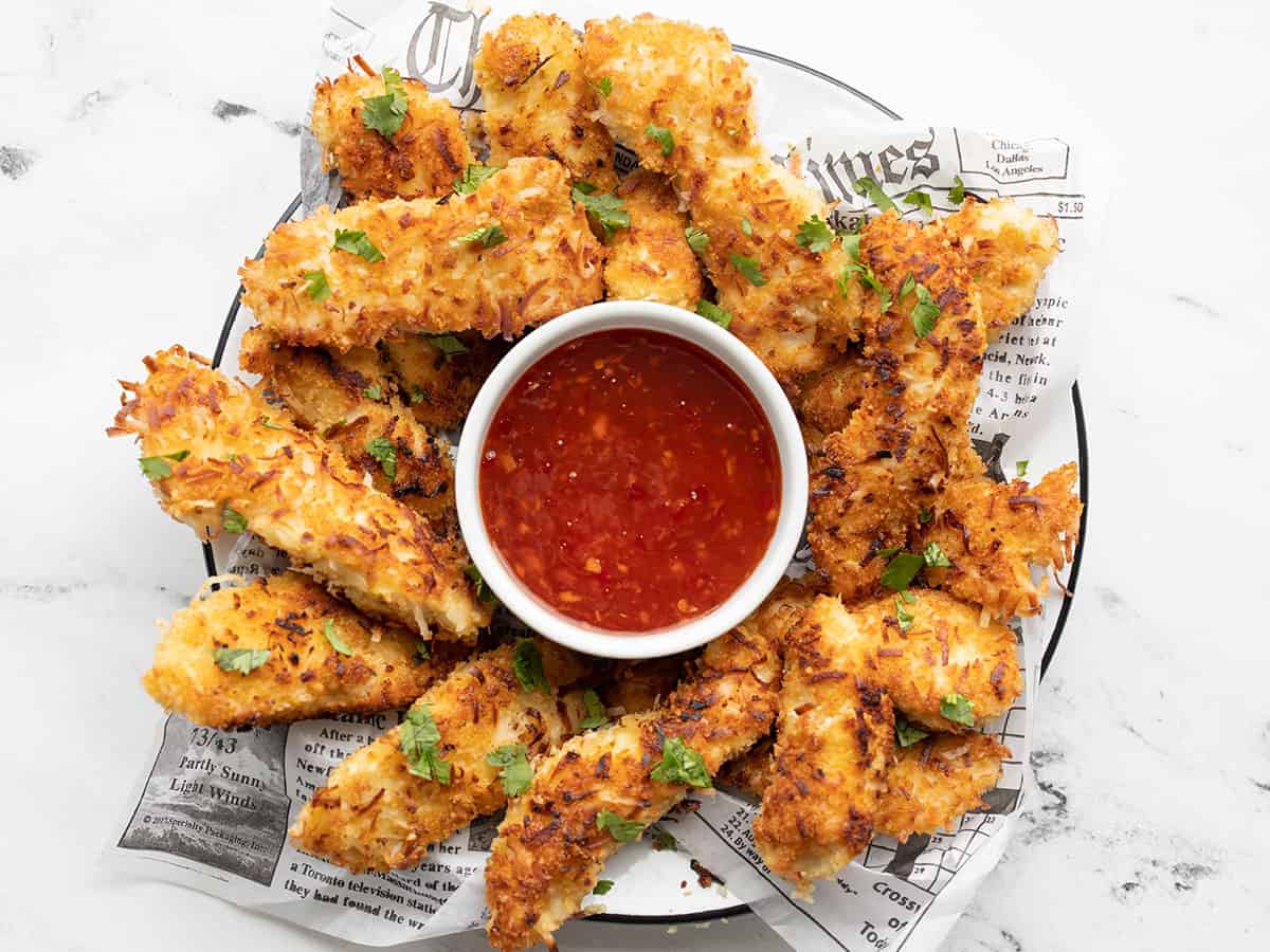 Overhead view of a plate full of coconut chicken strips with a bowl of sweet chili sauce in the center