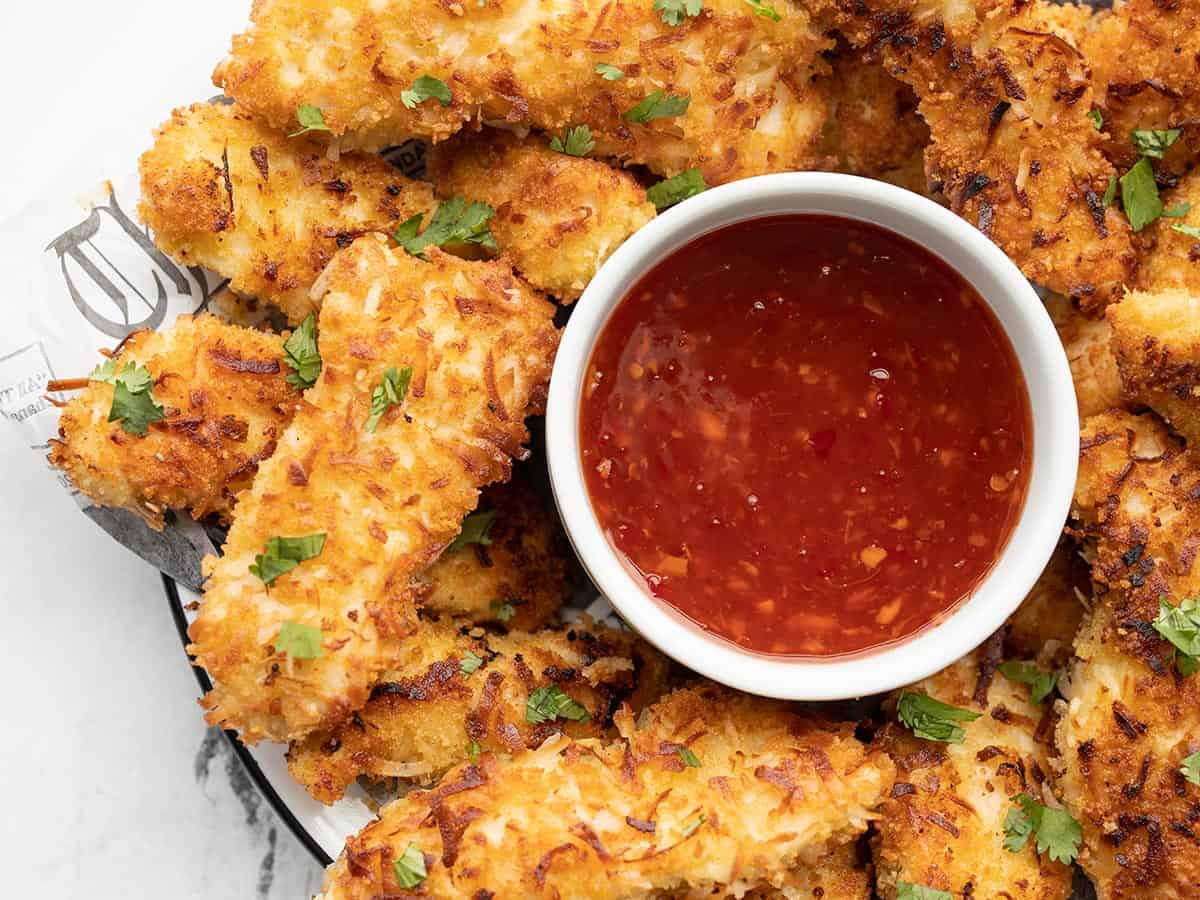 Close up of coconut chicken strips on a plate with a bowl of thai sweet chili sauce