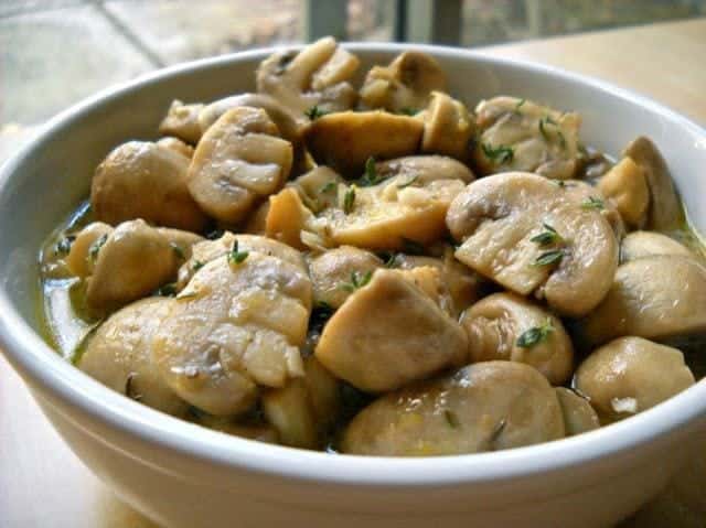 Bowl of marinated mushrooms with herbs.