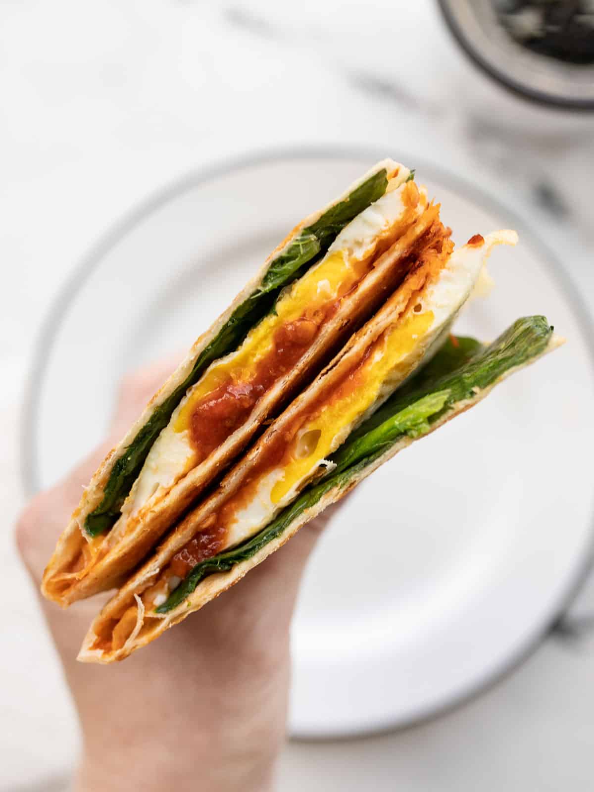 close up side view of a cut chili garlic breakfast quesadilla being held in a hand