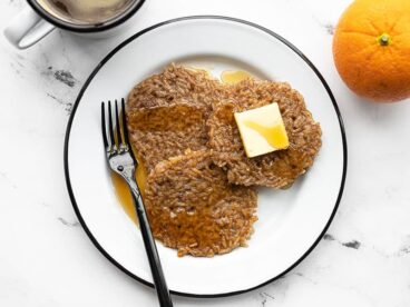 Overhead view of a plate with three rice pancakes, a cup of coffee and orange on the side