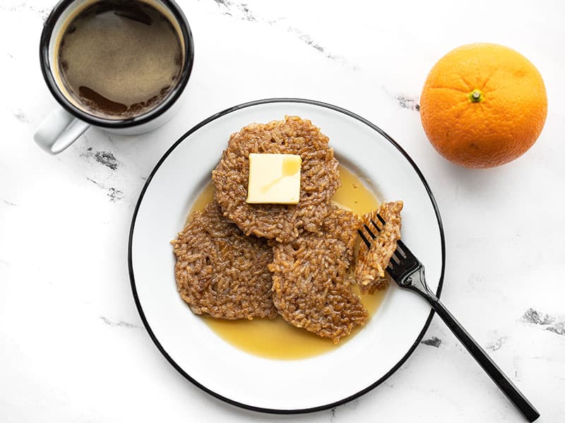 Rice pancakes on a plate with butter and maple syrup, a fork stuck through a bite of pancake. 