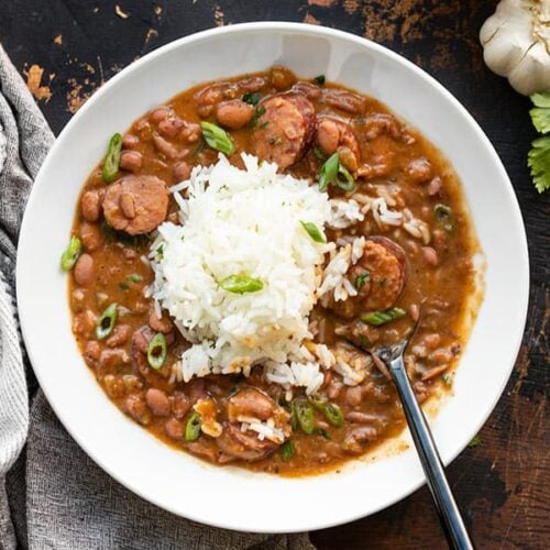 A bowl full of red beans and rice with sausage, a spoon in the center of the bowl