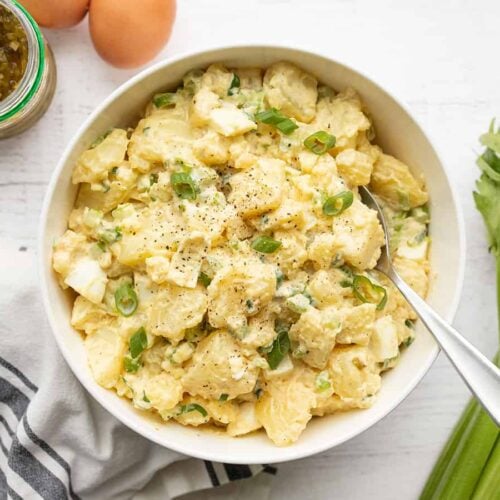 overhead view of a a bowl full of potato salad with celery, relish and eggs on the sides