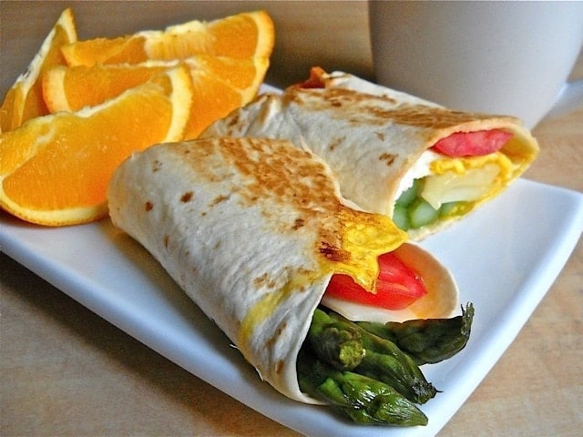 Asparagus breakfast wraps with cream cheese filling on a plate with oranges.