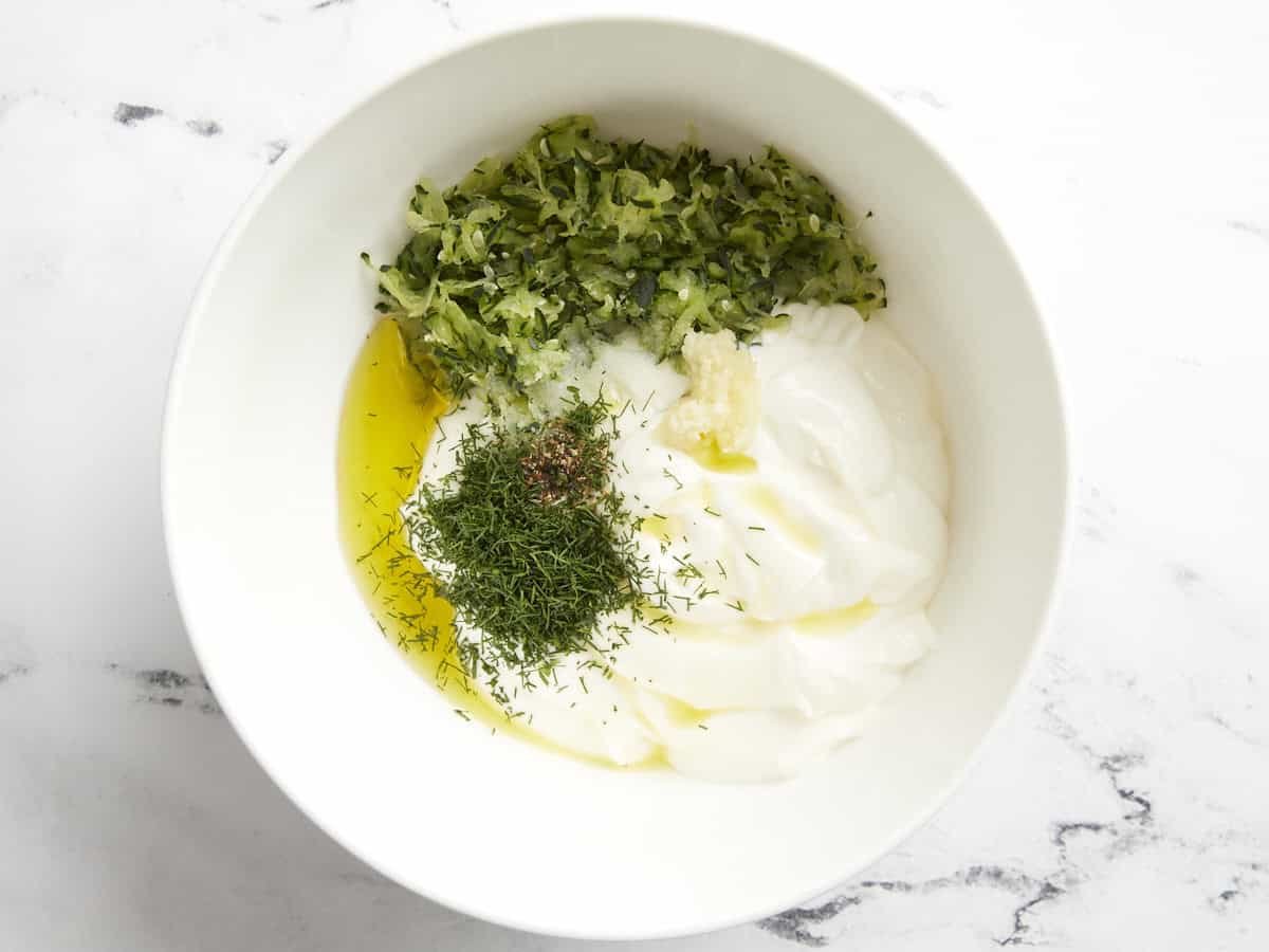 Tzatziki ingredients added to a mixing bowl.