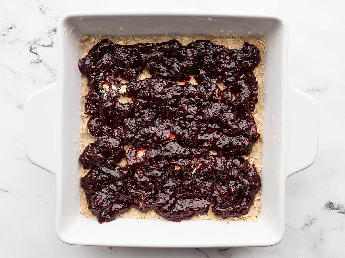 Jam spread out onto the oat mixture in the baking dish