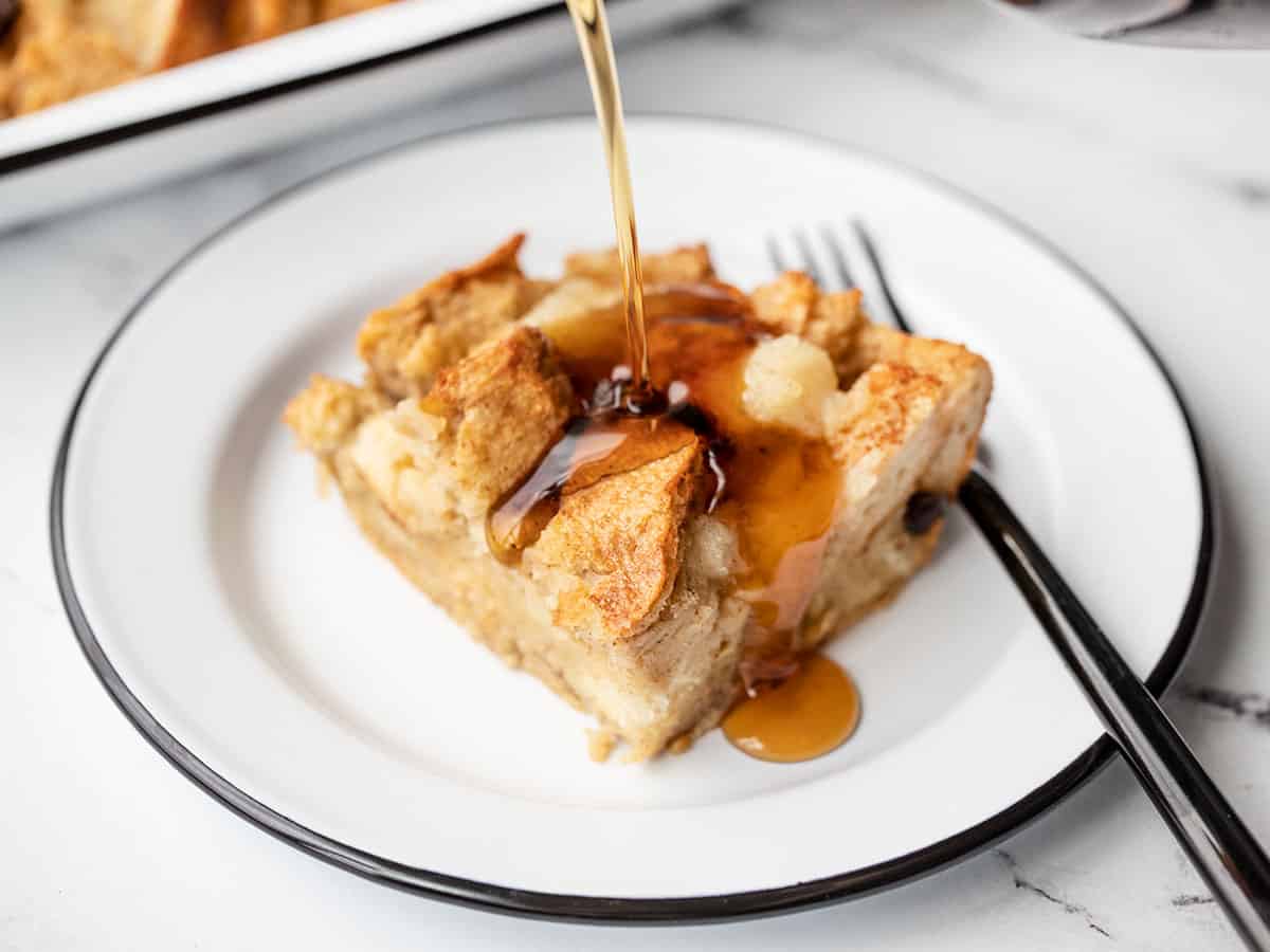 maple syrup being poured over a slice of apple cinnamon bread pudding