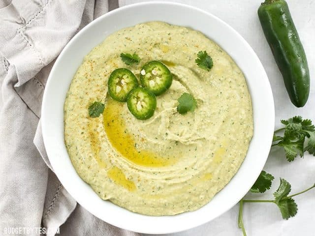 A bowl of jalapeño cilantro hummus with fresh jalapeño on the side