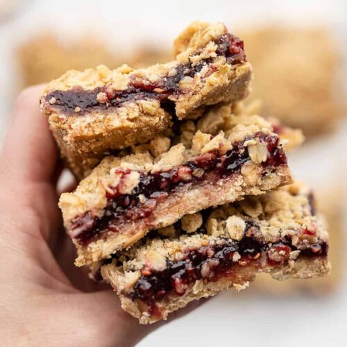 A hand holding a stack of raspberry oatmeal bars close to the camera