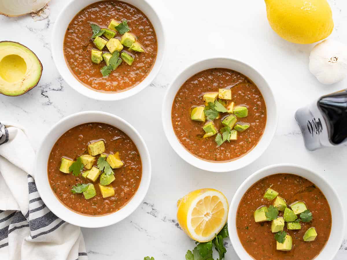 Four bowls of gazpacho topped with avocado and cilantro