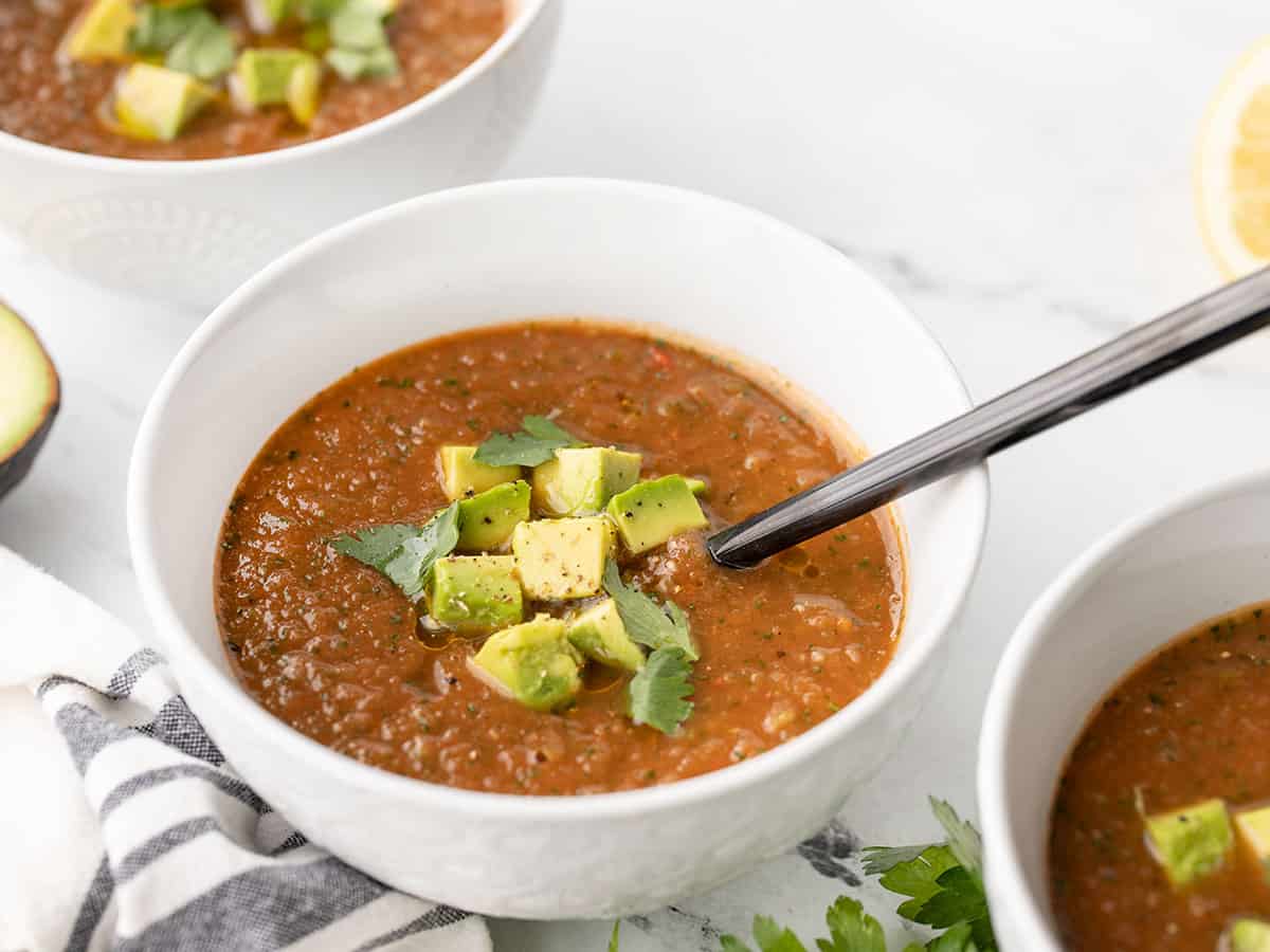 three bowls of gazpacho from the side, a spoon in one