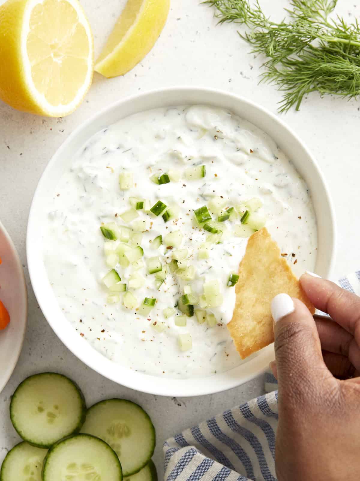 Overhead view of tzatziki sauce with a pita chip being dipped in the sauce.