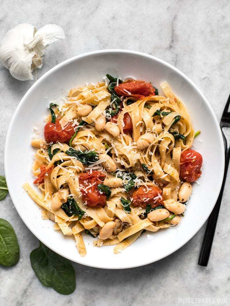 Overhead view of a large bowl full of Tuscan White Bean Pasta, spinach and garlic on the side