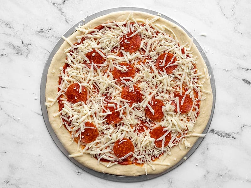 Cheese and pepperoni added to pizza dough