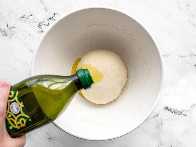 oil being poured onto a ball of dough in a mixing bowl.