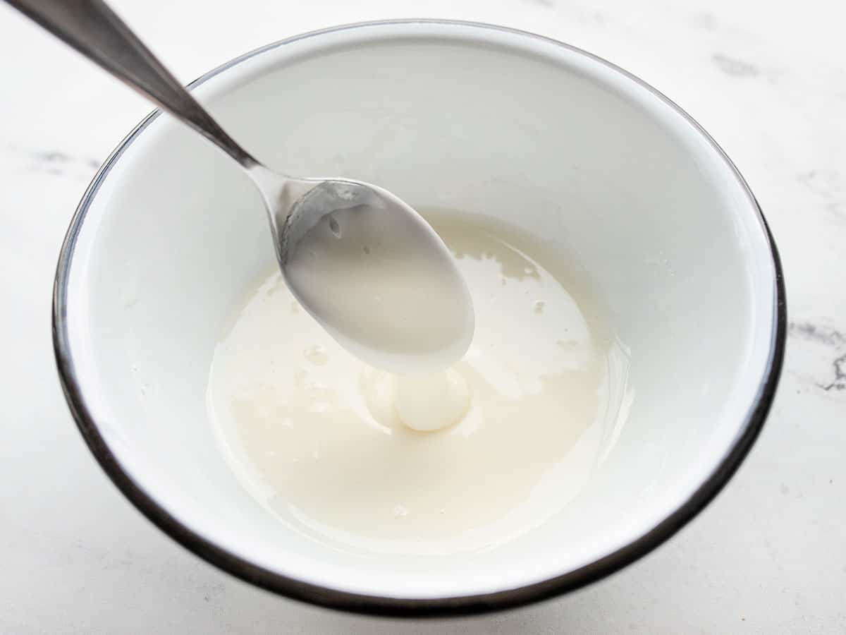 Mixed lemon glaze in a bowl, dripping off a spoon