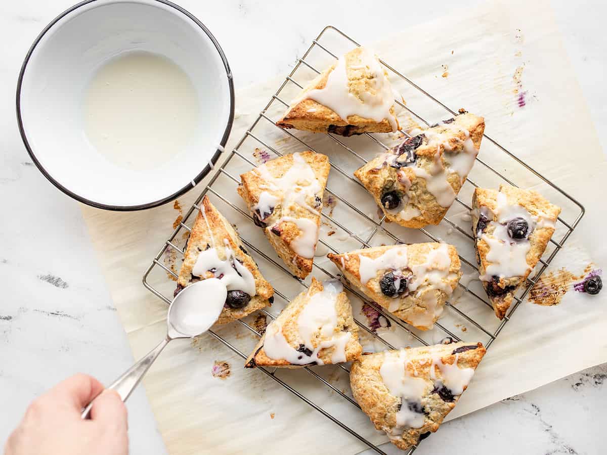 Lemon glaze being drizzled over scones on the cooling rack