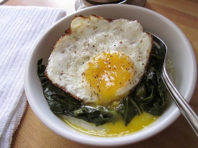 Plate of grits topped with greens and herbs served with a fork.