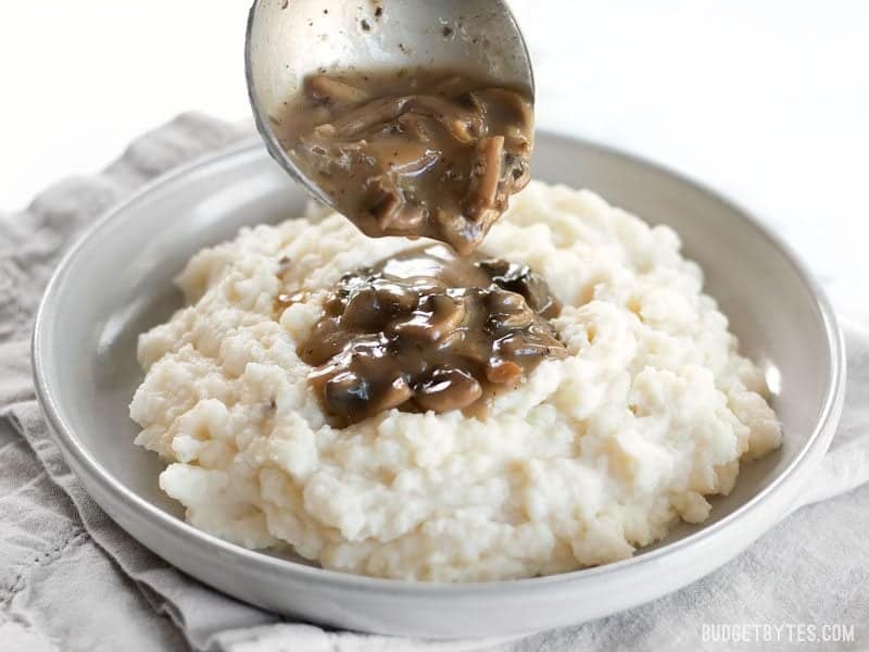 gravy being poured onto mashed potatoes on plate 