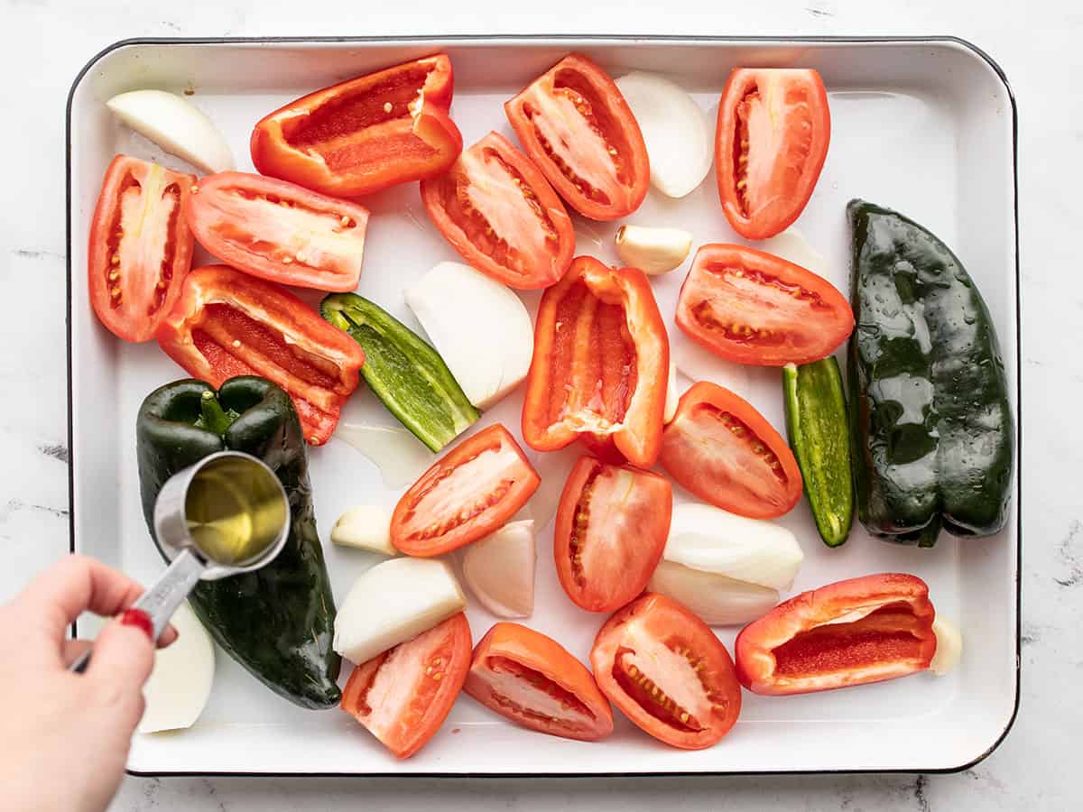 prepped vegetables on a baking sheet with oil being drizzled over top