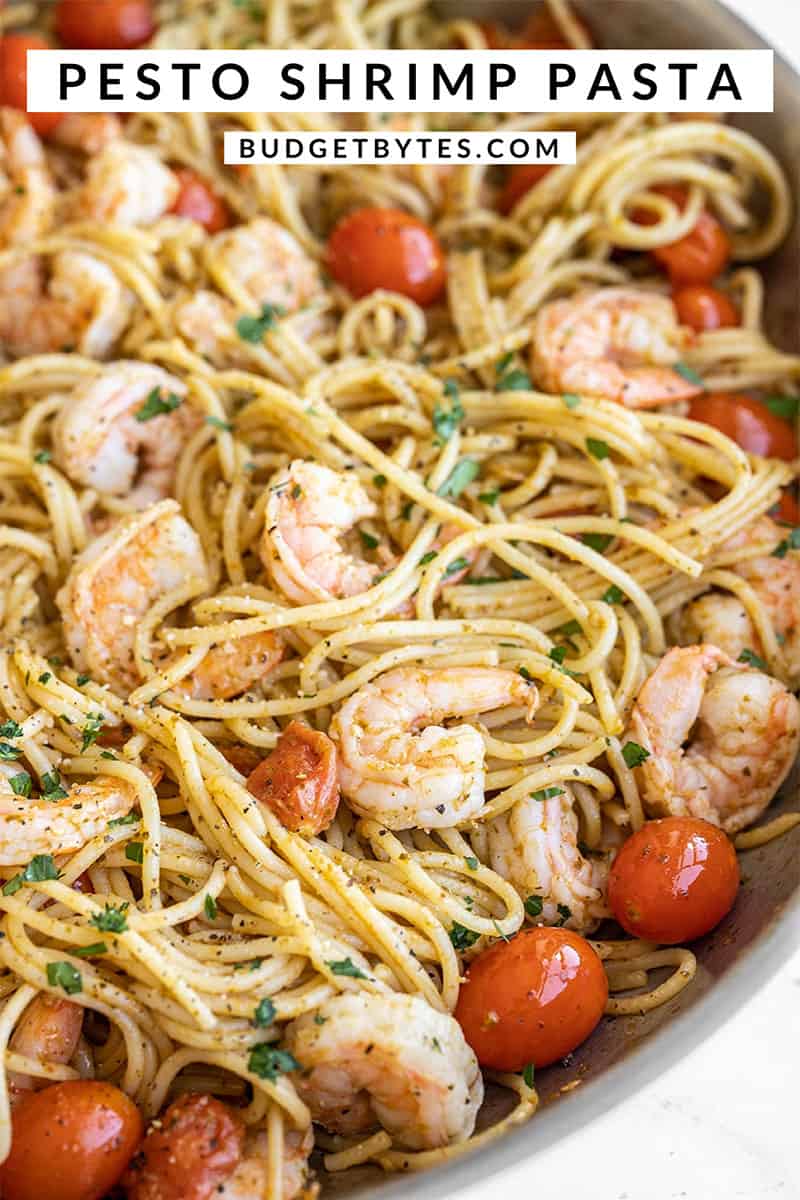 Close up side view of a skillet full of pesto shrimp pasta with title text at the top