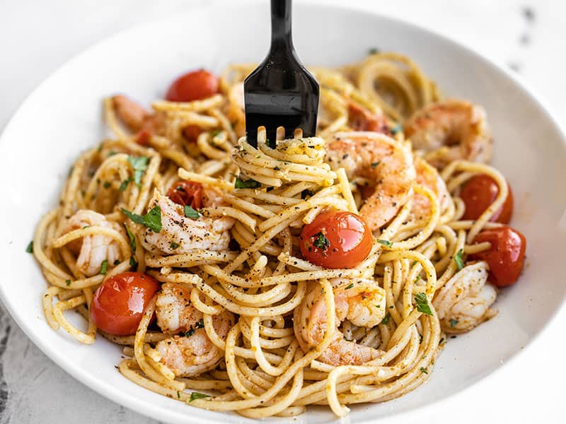 Front view of a bowl full of pesto shrimp pasta with a fork twirling the pasta in the center