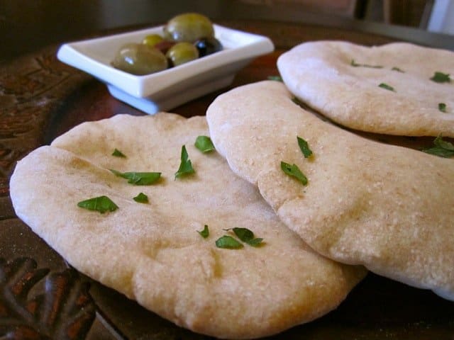 Whole pita bread displayed on a wooden board.