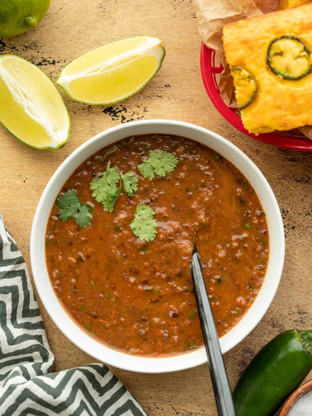 Overhead view of a bowl of black bean and roasted salsa soup, cornbread and limes on the side