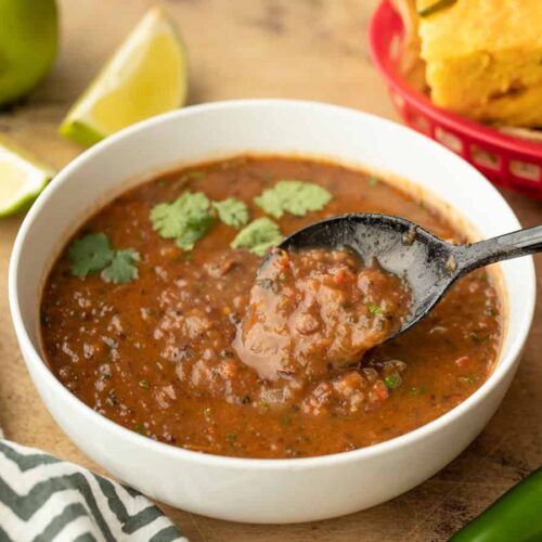 Side view of black bean and roasted salsa soup in a bowl with a spoon in the center