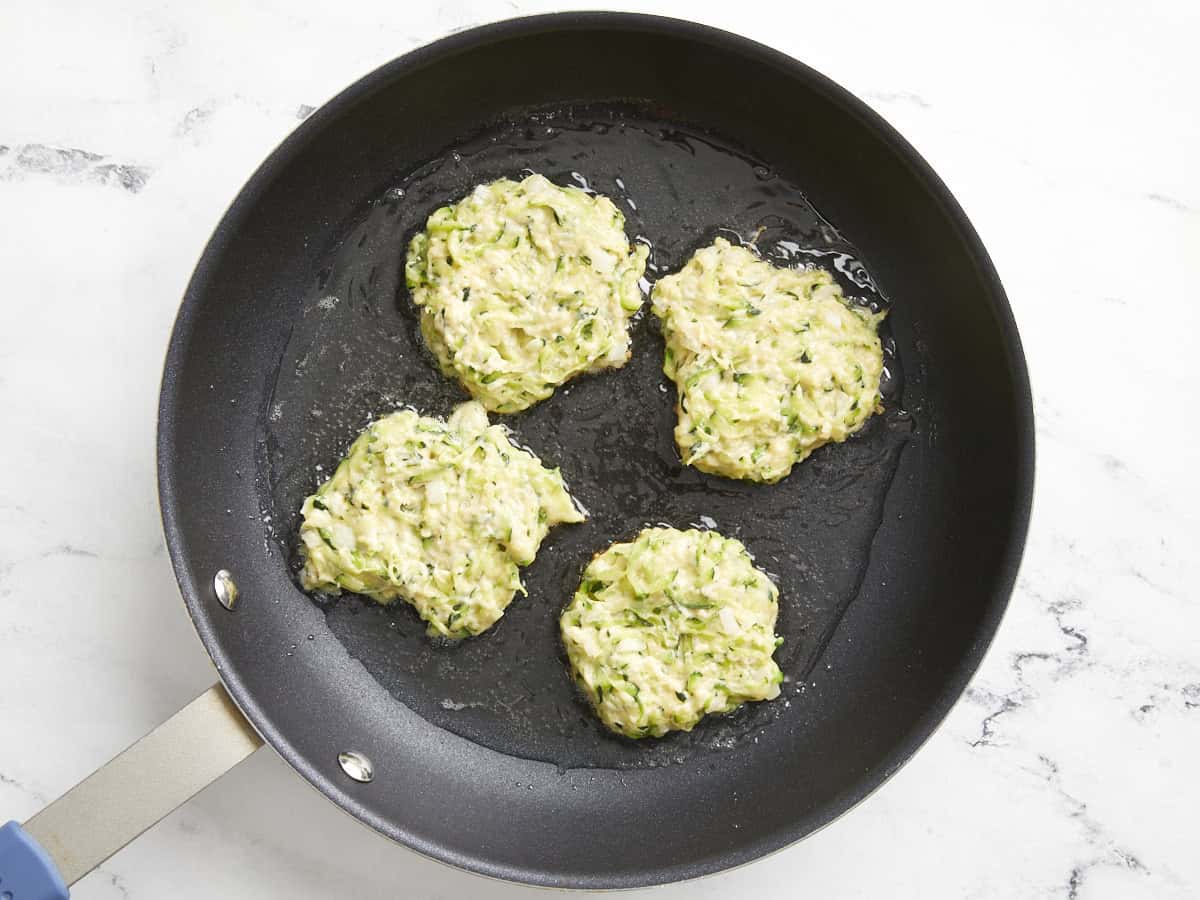 zucchini fritters added to hot oil in pan.