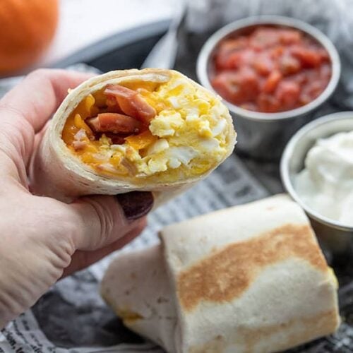 A hand holding half of a breakfast burrito with the open cut side facing the camera.