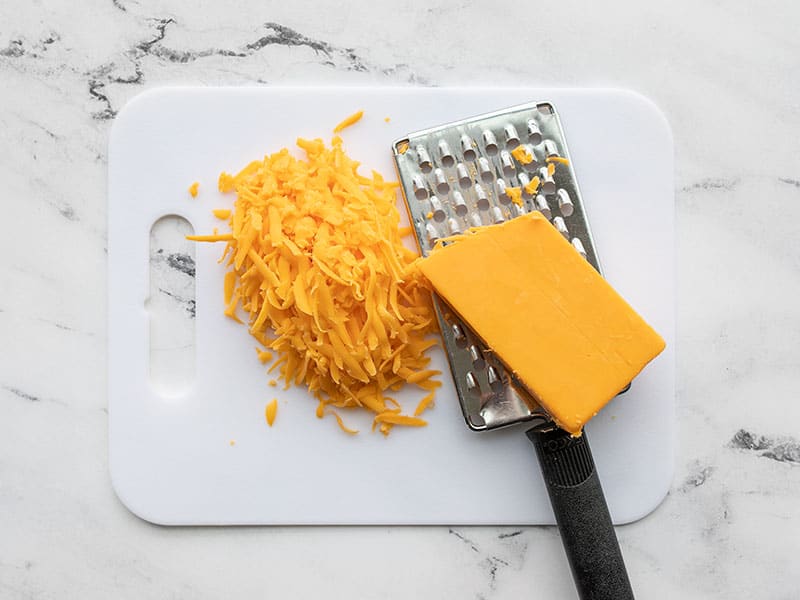 Shredded cheddar on a cutting board with the cheese grater.