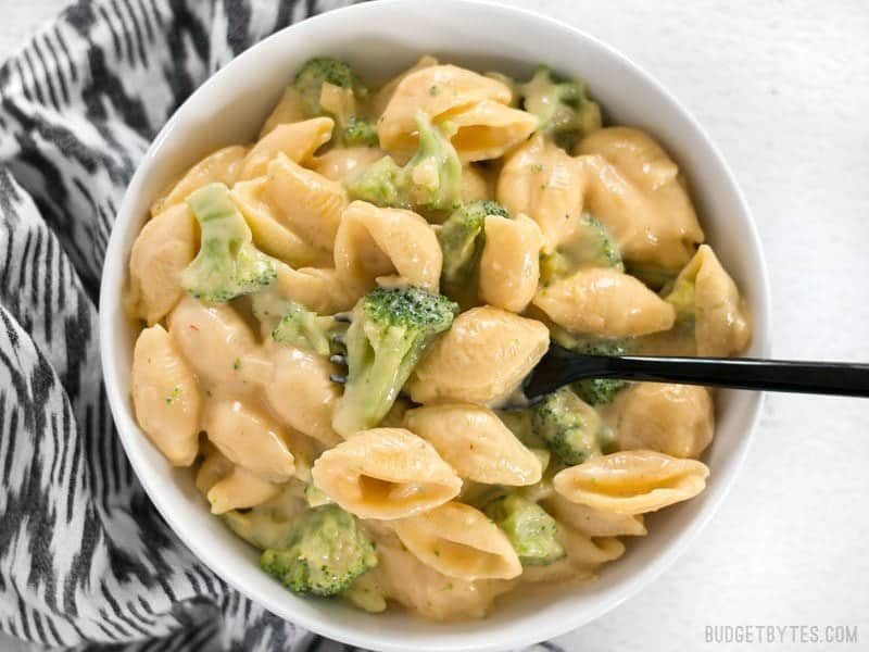 Top view of a bowl of Broccoli shells n' cheese sitting on a black and white patterned napkin 