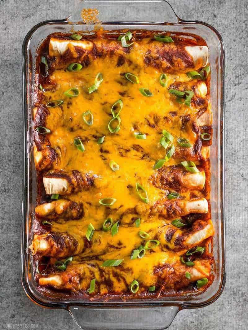 A full casserole dish of Chorizo and Sweet Potato Enchiladas with melted cheese and garnished with green onion