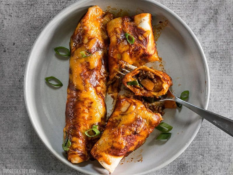 Two Chorizo and Sweet Potato enchiladas on a plate being eaten with a fork