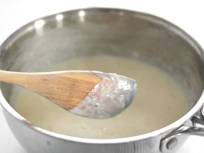 Thickened White cheese sauce, wooden spoon holding up a spoonful 