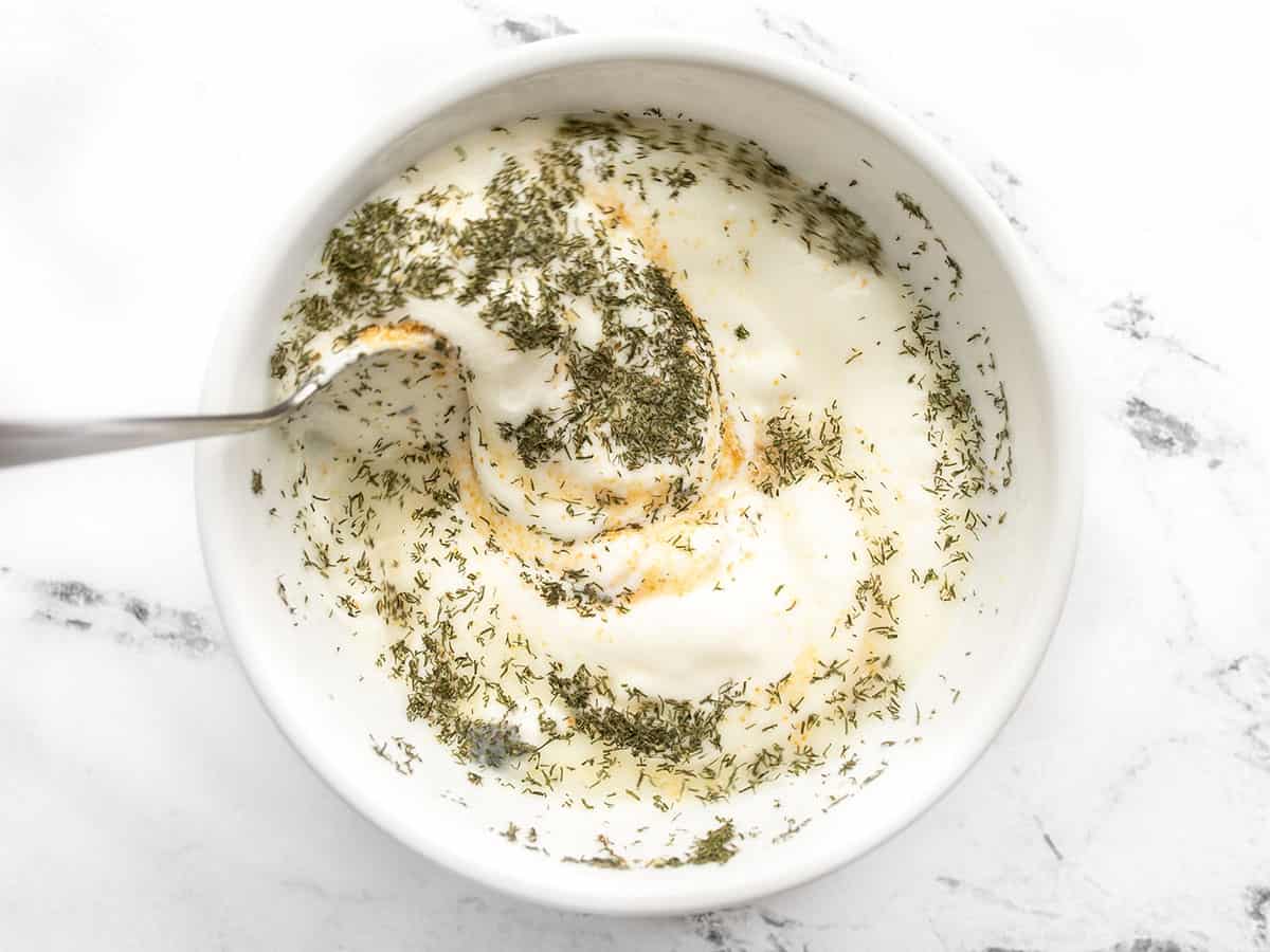 lemon, garlic powder, and dried dill being stirred into yogurt