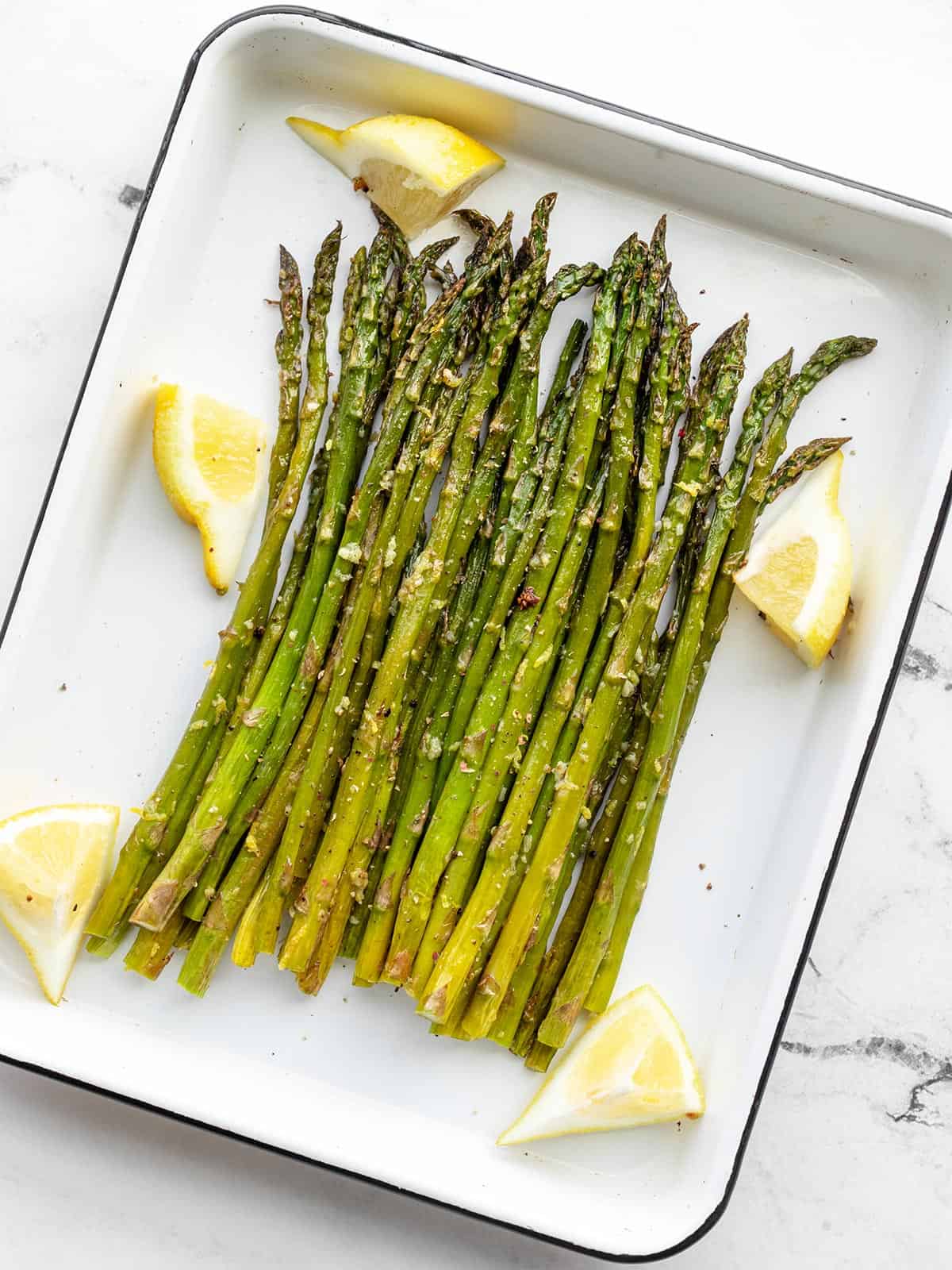 Lemon Garlic Roasted Asparagus on a white roasting pan with lemon wedges