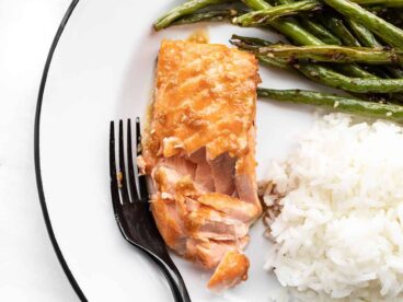 a flaked piece of baked ginger salmon on a plate with green beans and rice