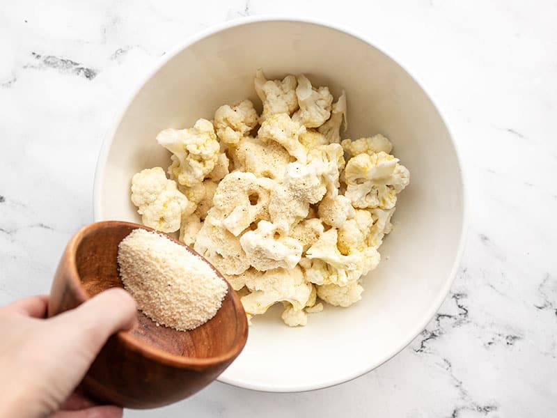 Seasoning being sprinkled over cauliflower in a bowl