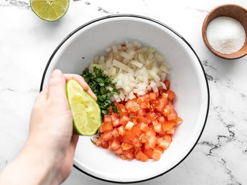 Lime being squeezed over the bowl of vegetables.