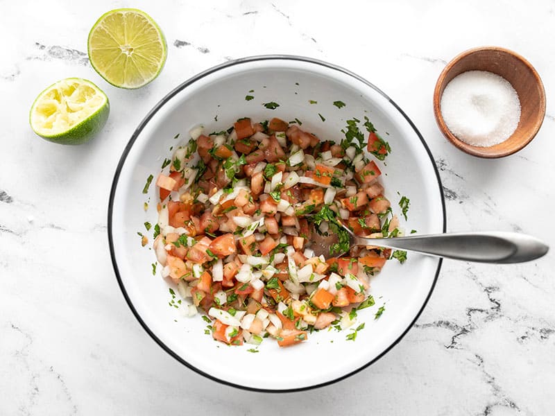 Stirred pico de gallo in the bowl, salt and limes on the side.