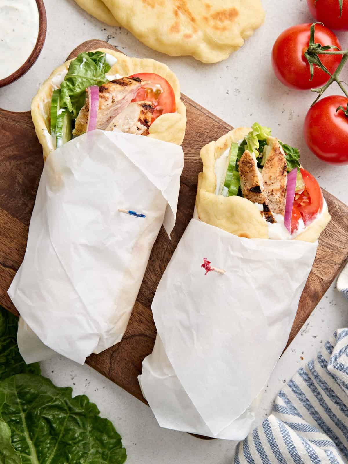 A magical blend of yogurt, lemon, and mediterranean spices makes this homemade chicken shawarma mouthwateringly delicious. Step by step photos. Overhead view of two chicken shawarma wraps on a wooden cutting board.
