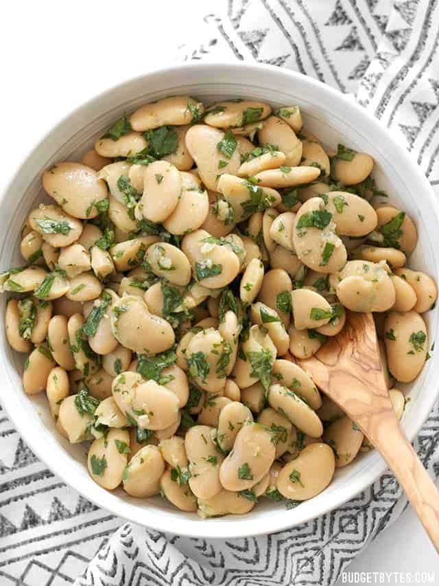 Top view of Marinated White Beans in white bowl with wooden serving spoon 